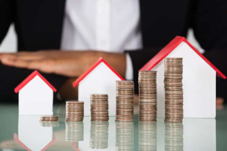 Businesswoman With House Model And Stacked Coins On Desk