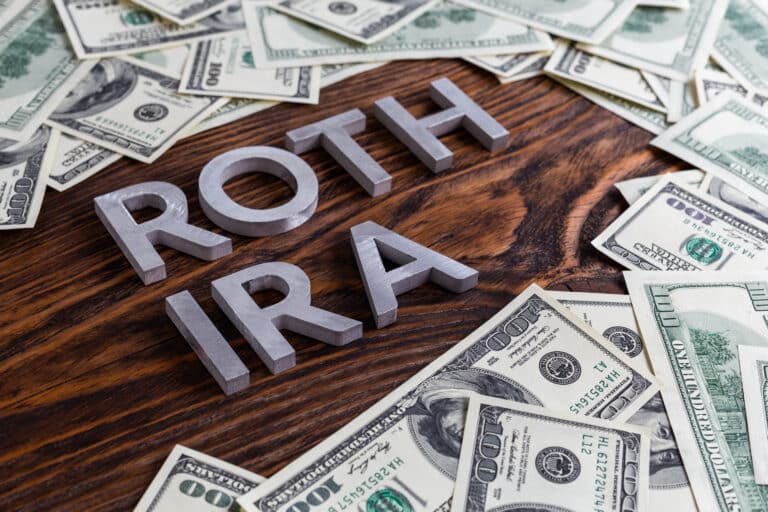 words ROTH IRA laid on wooden surface by metal letters with us dollar banknotes